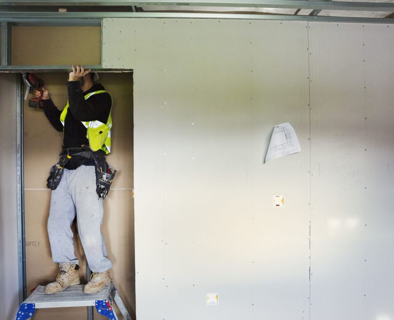 A carpenter in work clothes on a construction site, using an electric drill. ,Construction Site,England A carpenter in work clothes on a construction site, using an electric drill.